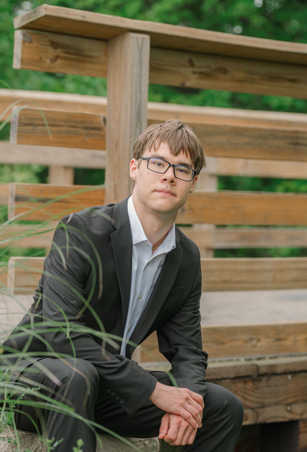 senior leaning in front of a fence in his suit