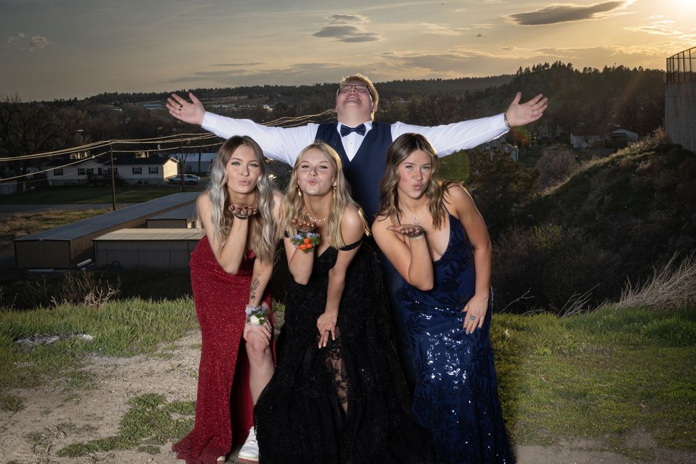 Friends in elegant prom attire pose outdoors at sunset, bathed in warm golden light, capturing joy and unforgettable memories.