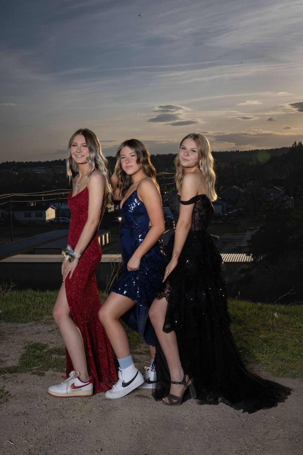 Friends in elegant prom attire pose outdoors at sunset, bathed in warm golden light, capturing joy and unforgettable memories.
