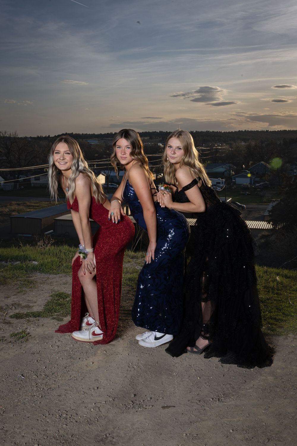 Friends in elegant prom attire pose outdoors at sunset, bathed in warm golden light, capturing joy and unforgettable memories.