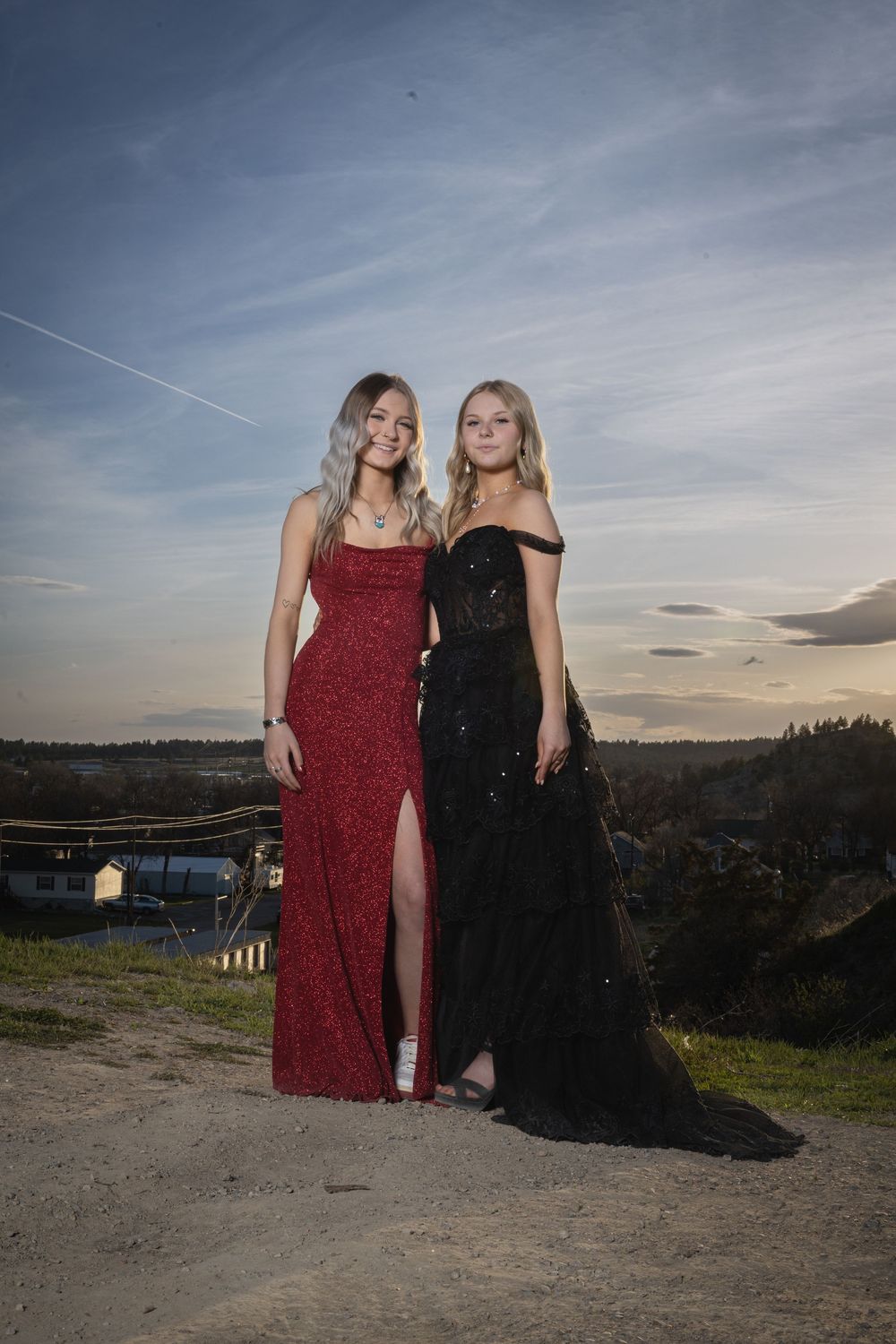 Sisters in elegant prom attire pose outdoors at sunset, bathed in warm golden light, capturing joy and unforgettable memories.