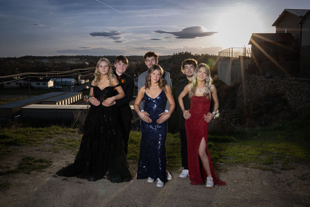 Friends in elegant prom attire pose outdoors at sunset, bathed in warm golden light, capturing joy and unforgettable memories.