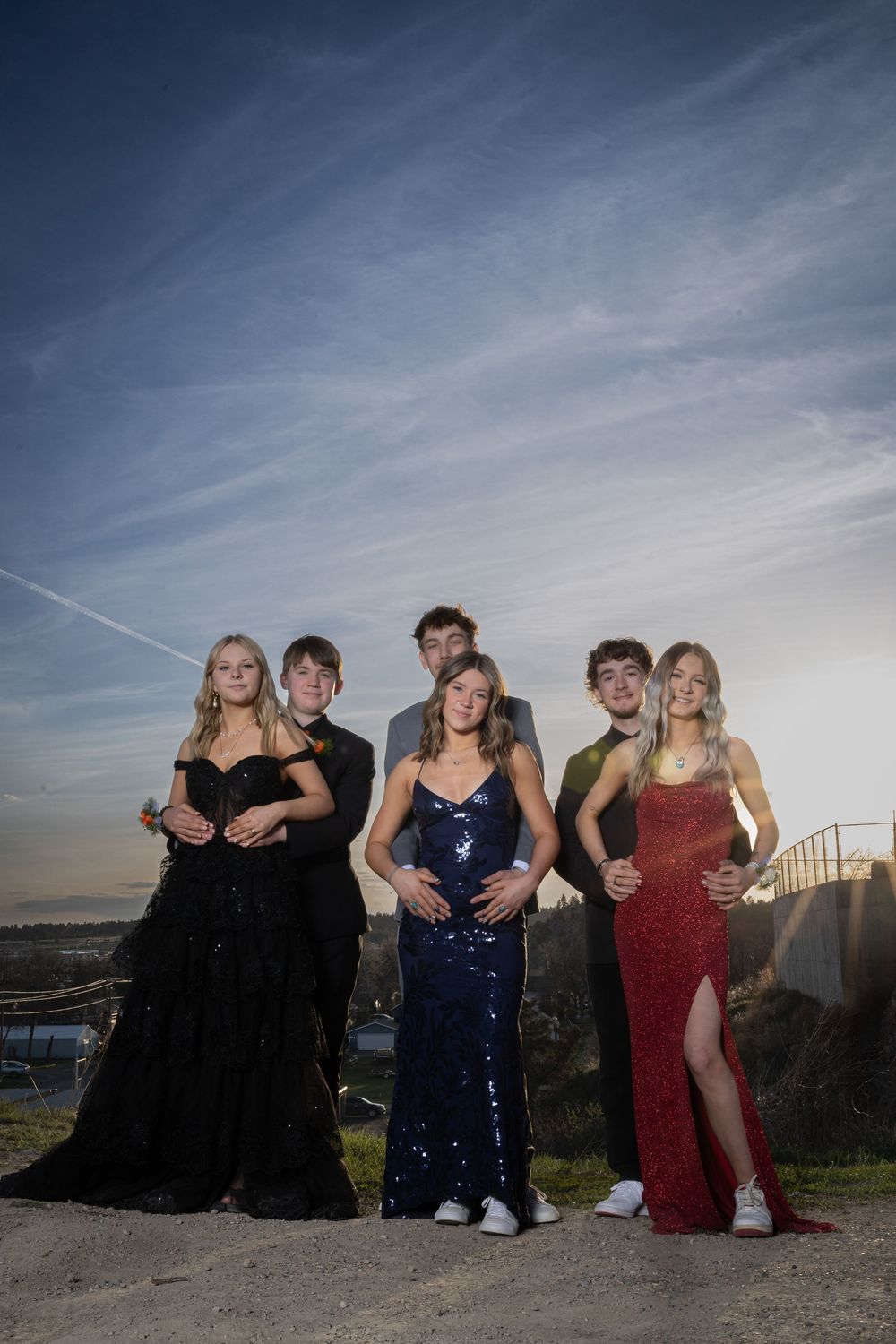 Friends in elegant prom attire pose outdoors at sunset, bathed in warm golden light, capturing joy and unforgettable memories.