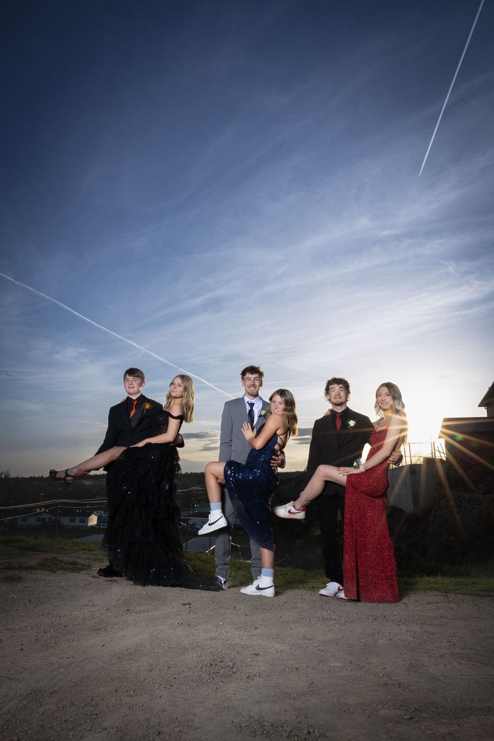 Friends in elegant prom attire pose outdoors at sunset, bathed in warm golden light, capturing joy and unforgettable memories.