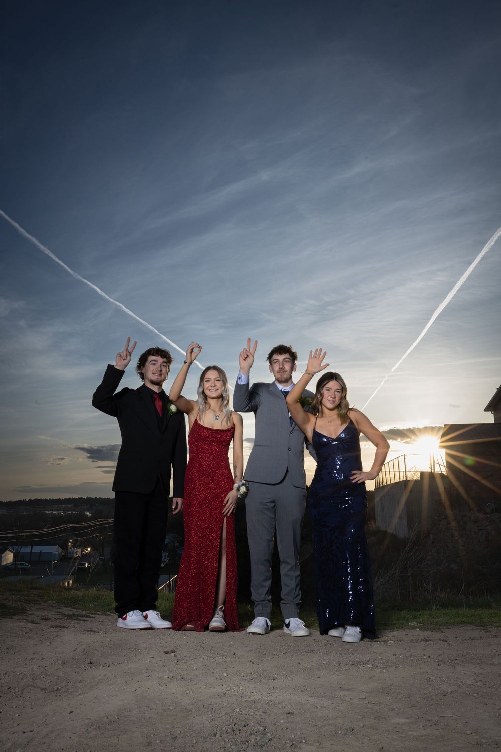 Friends in elegant prom attire pose outdoors at sunset, bathed in warm golden light, capturing joy and unforgettable memories.