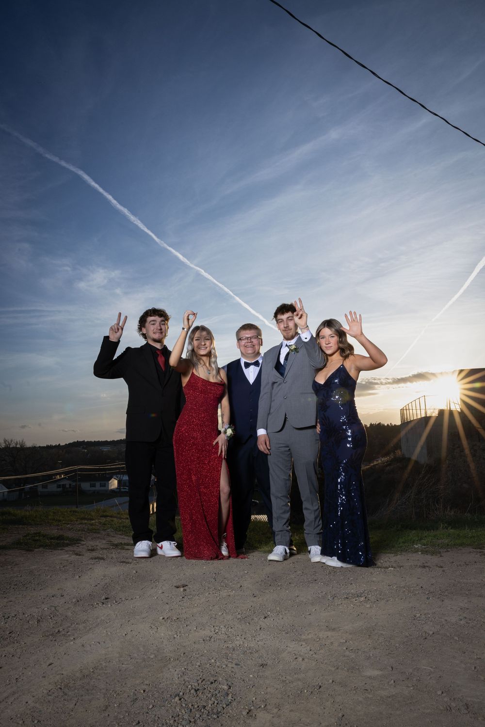 Friends in elegant prom attire pose outdoors at sunset, bathed in warm golden light, capturing joy and unforgettable memories.