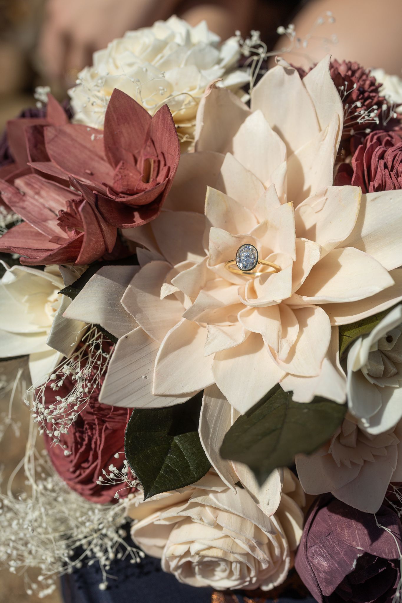 Close-up of cream and mauve floral bouquet with engagement ring on center flower in soft natural lighting.