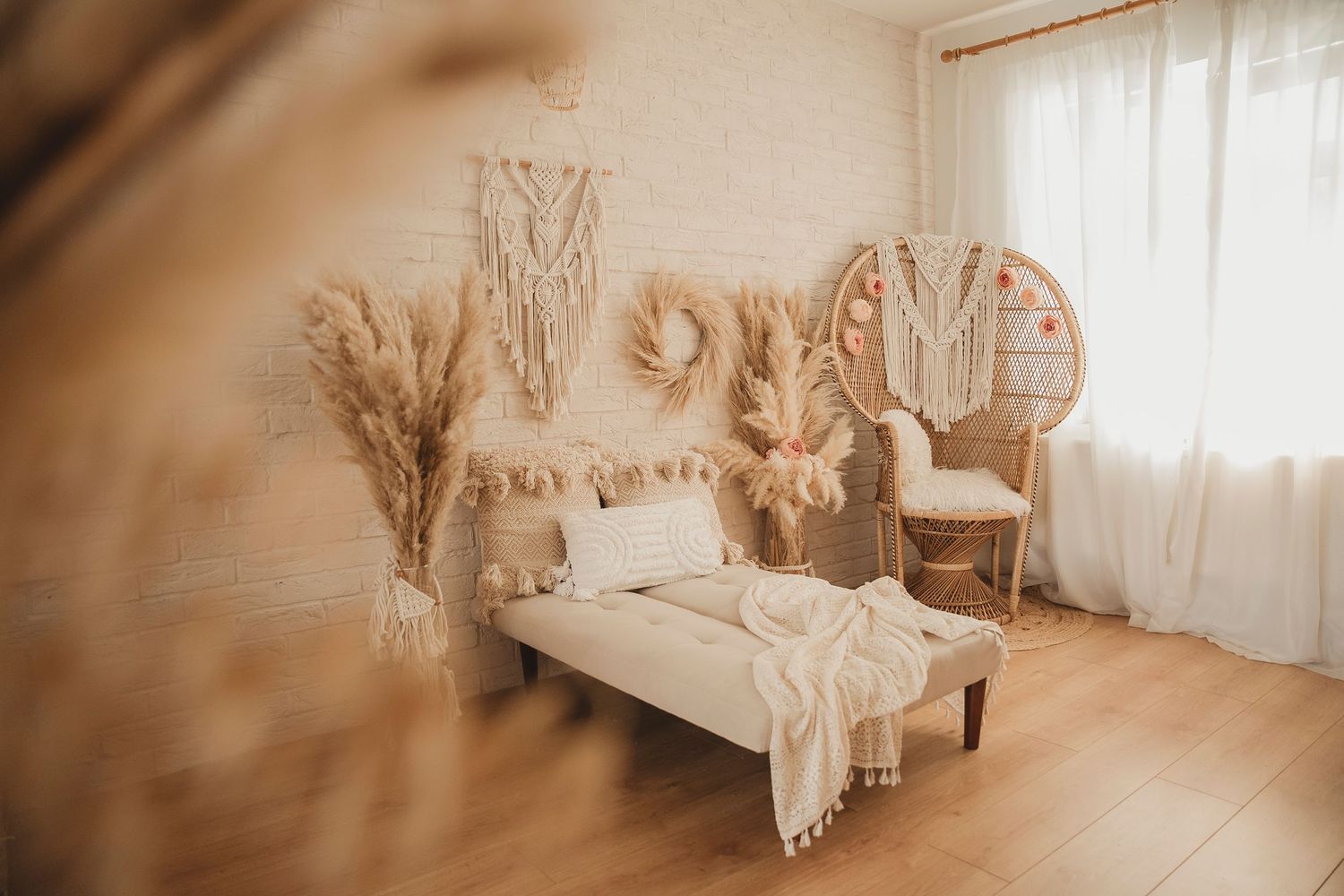 Bohemian bedroom with peacock chair, macrame wall hangings, pampas grass arrangements and white bedding on wood floors.