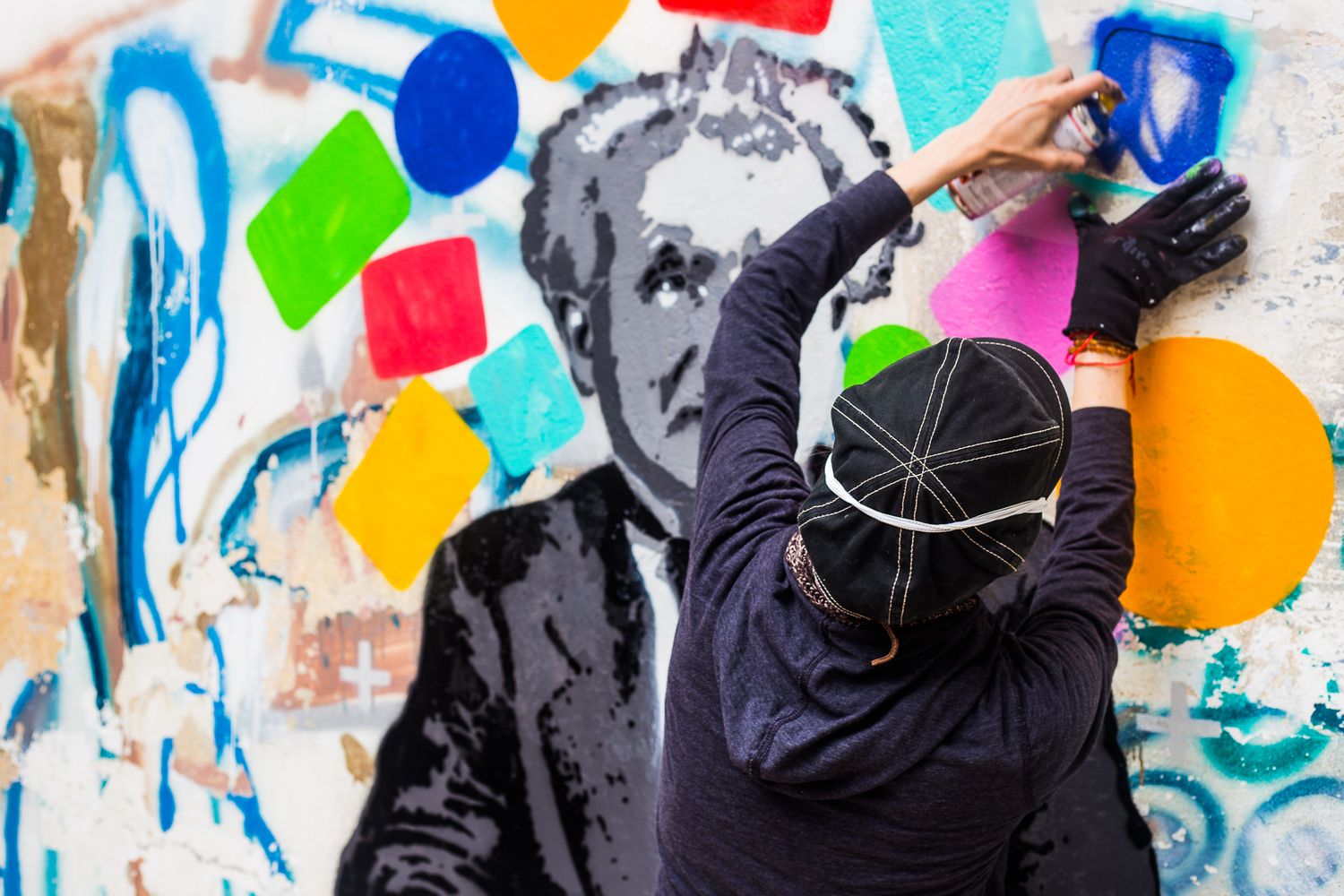 People spray painting colorful graffiti art on a wall covered in bright dots and patterns.