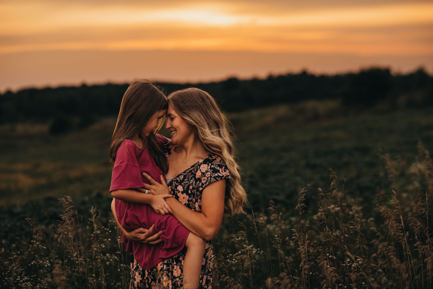 Two people share an intimate embrace in a wildflower field at sunset with golden light illuminating the scene.