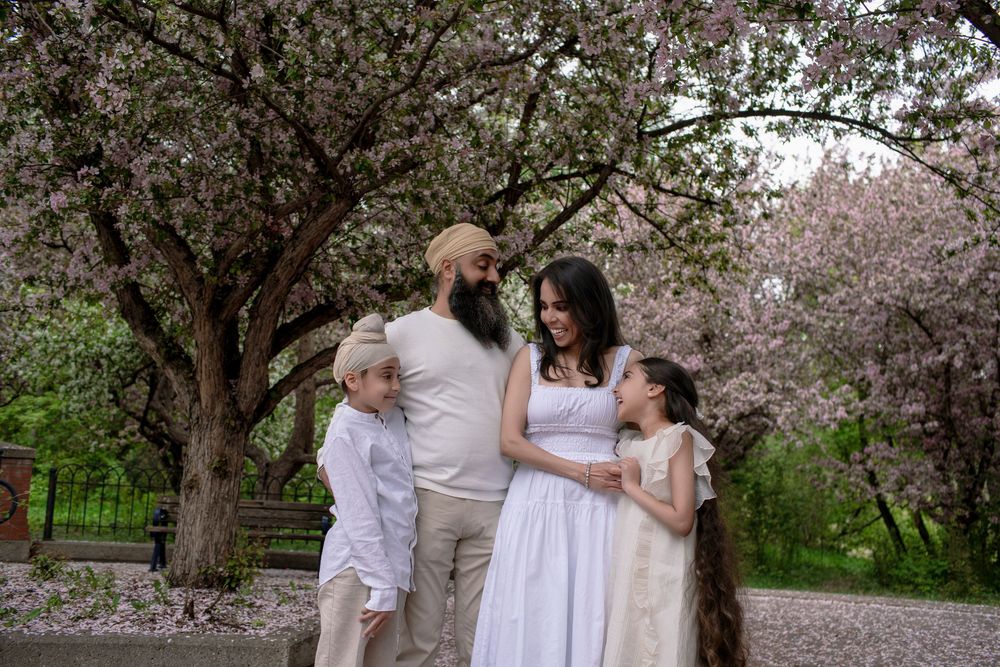 Family of four poses under blooming cherry blossom trees in a park during spring.