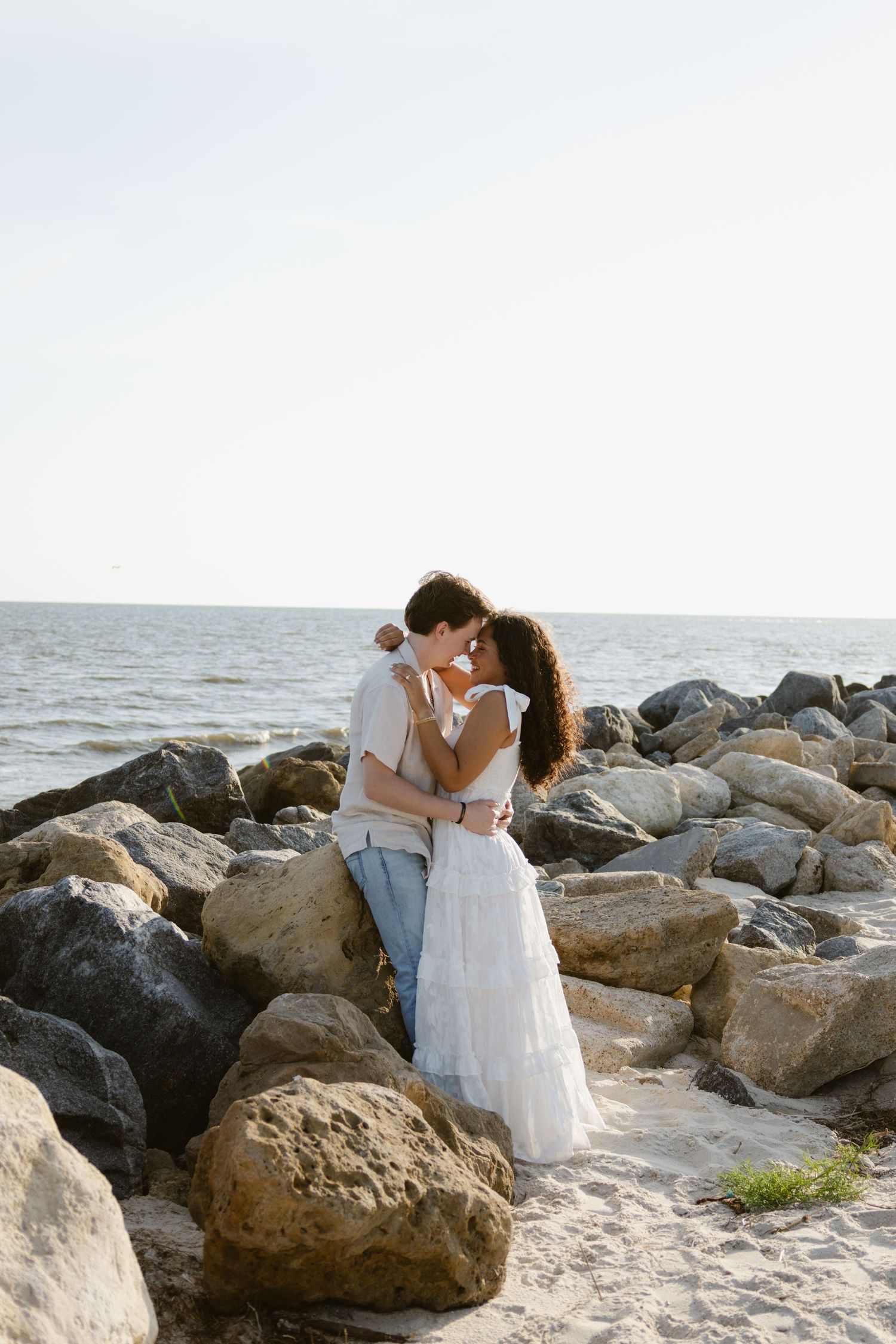 A couple during their engagement, leaned against rocks on a beach in Florida.