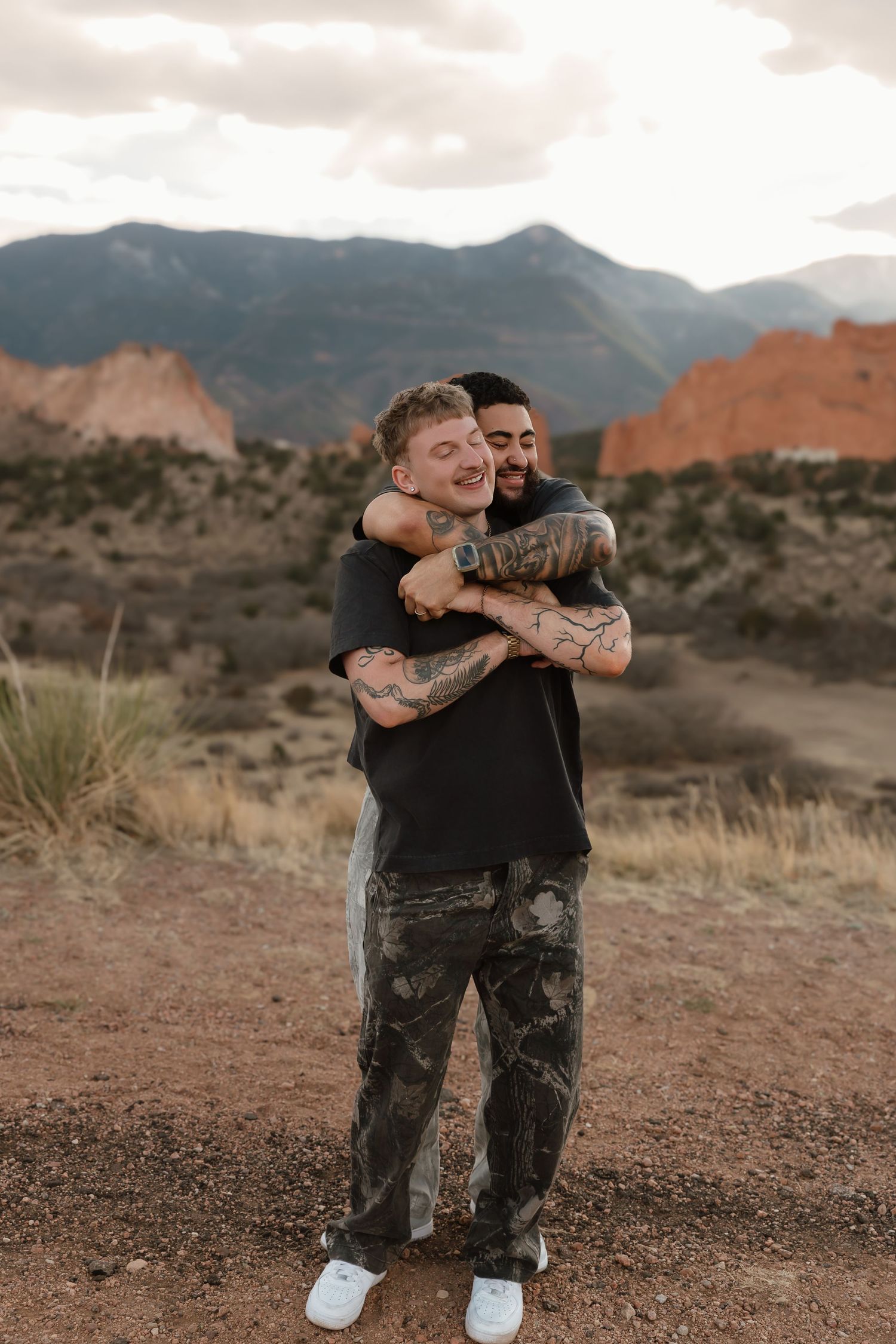 Two people embrace outdoors with Garden of the Gods rock formations and mountains in the background in Colorado.