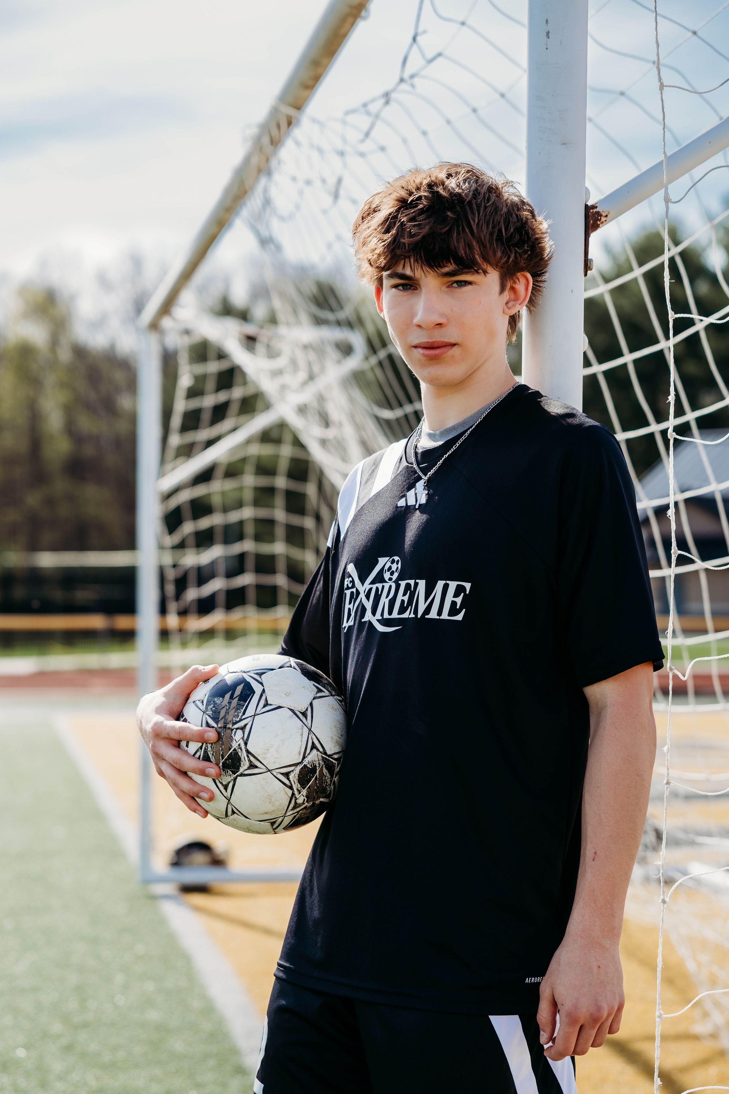 Soccer player in black tshirt standing near goal post on soccer field during practice session.