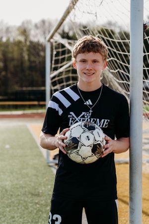 Soccer player holding a worn soccer ball while standing in front of goal net on artificial turf field.