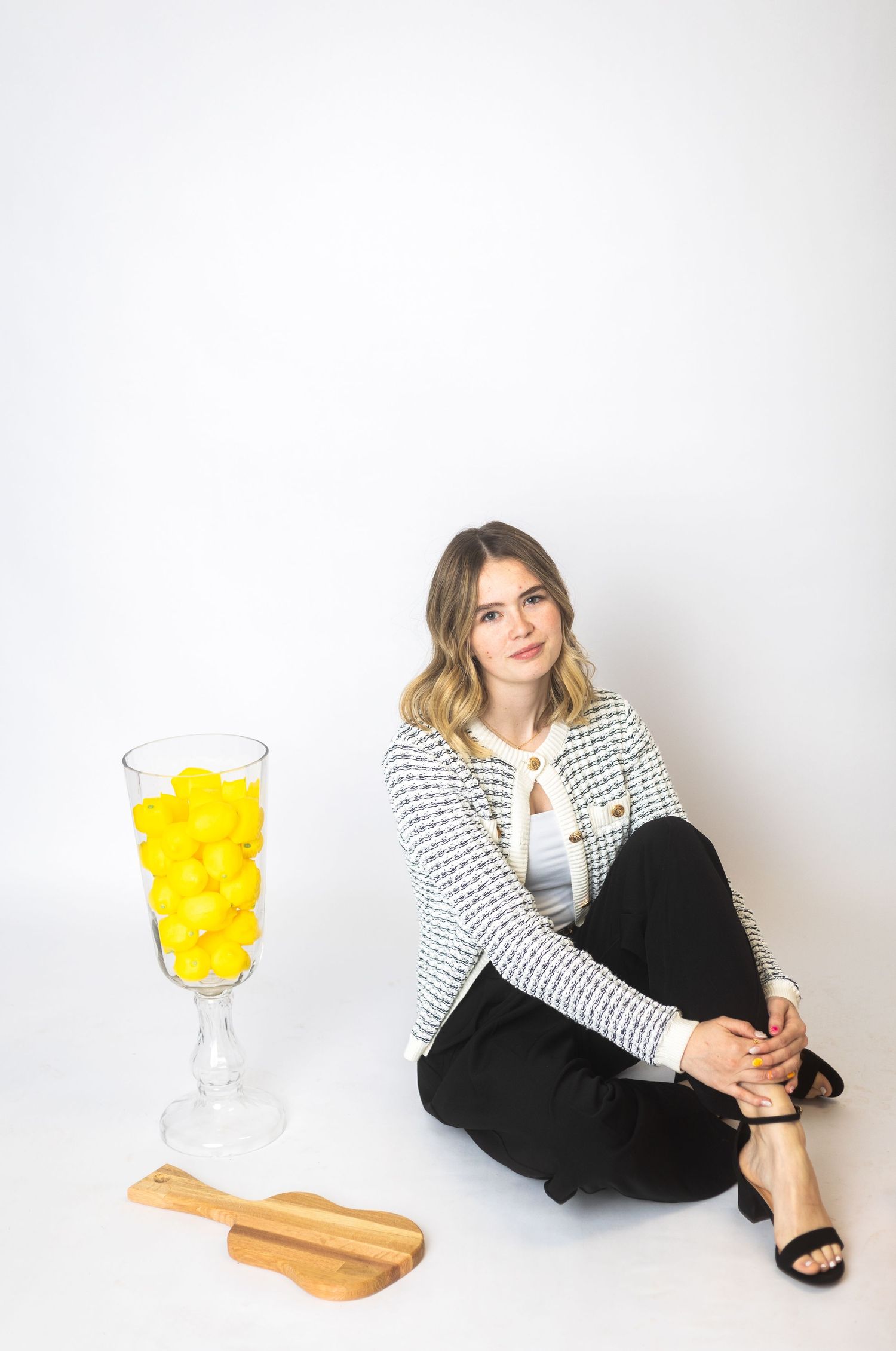 Person sitting casually next to large yellow cocktail on white background.