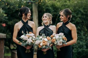 Wedding party holding elegant white and peach floral bouquets in an outdoor garden setting.
