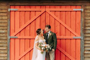 Wedding portraits against a vibrant orange barn door create striking rustic backdrop.