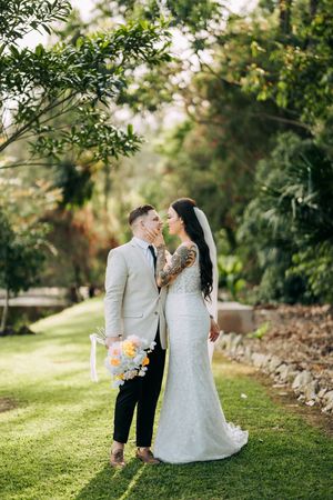 Newlyweds pose for portraits on a grassy hillside surrounded by lush greenery.