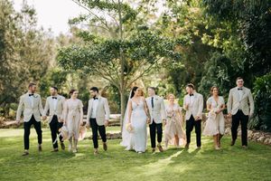 Wedding party lined up for group photos on a sunny lawn with trees in background.