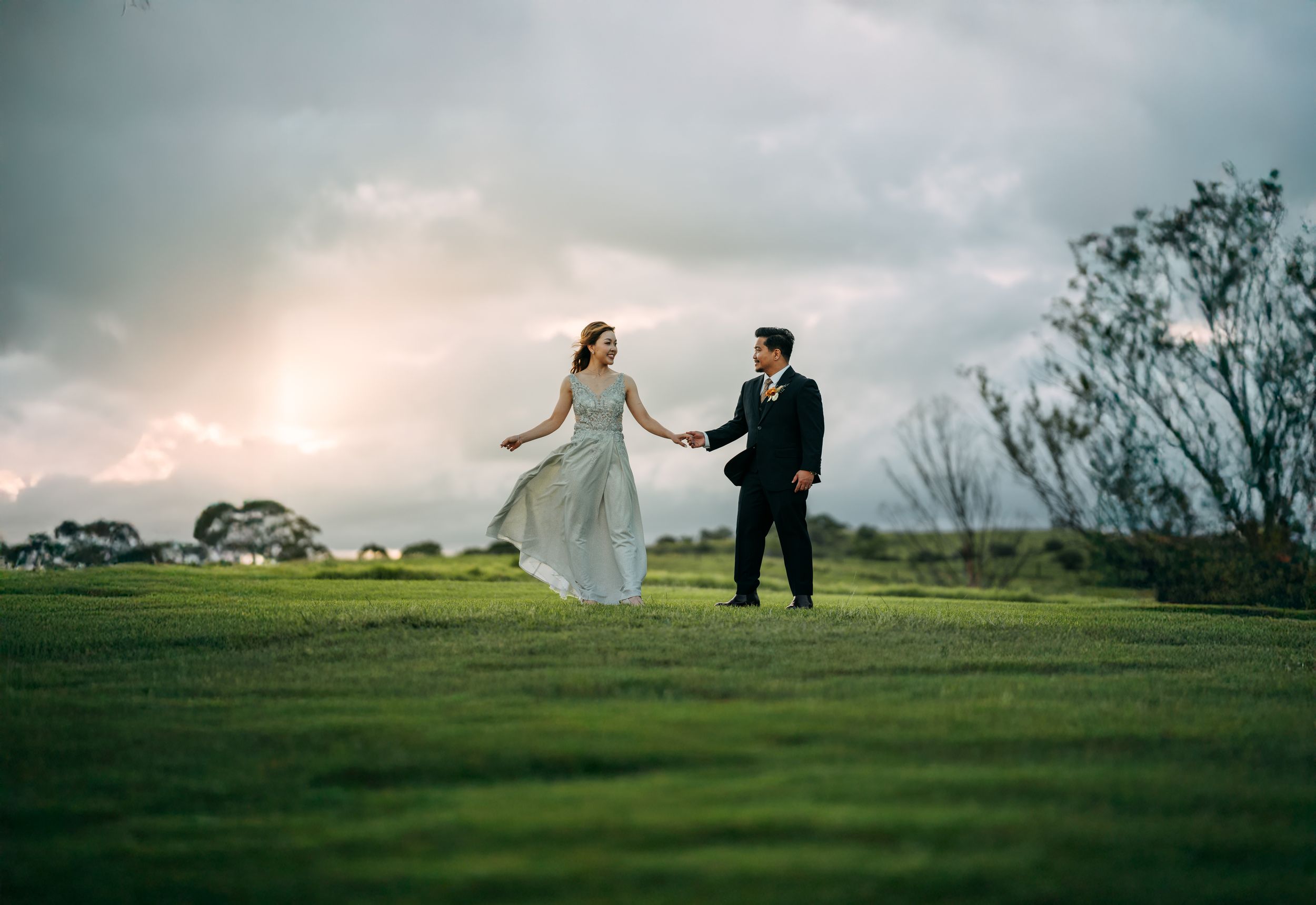 A couple walks together across a grassy hilltop during golden hour.