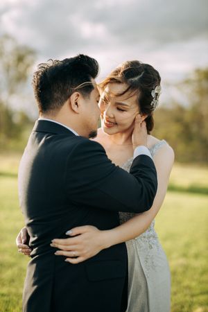 A couple embraces in a sunny field wearing wedding attire.