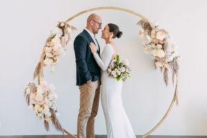 An elegant wedding scene with a circular floral arch decorated with blush roses and dried flowers.