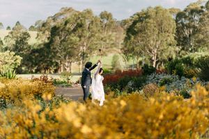 Couple embraces in a field of golden wildflowers during sunset with mountains in the background.