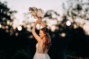 A celebratory moment at sunset with a bouquet raised against a backdrop of twinkling lights.