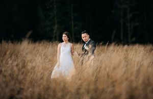 A romantic portrait in tall golden grass with a dark forest backdrop.