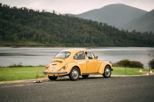 A bright yellow vintage Volkswagen Beetle parked by a scenic lake with mountains in the background.
