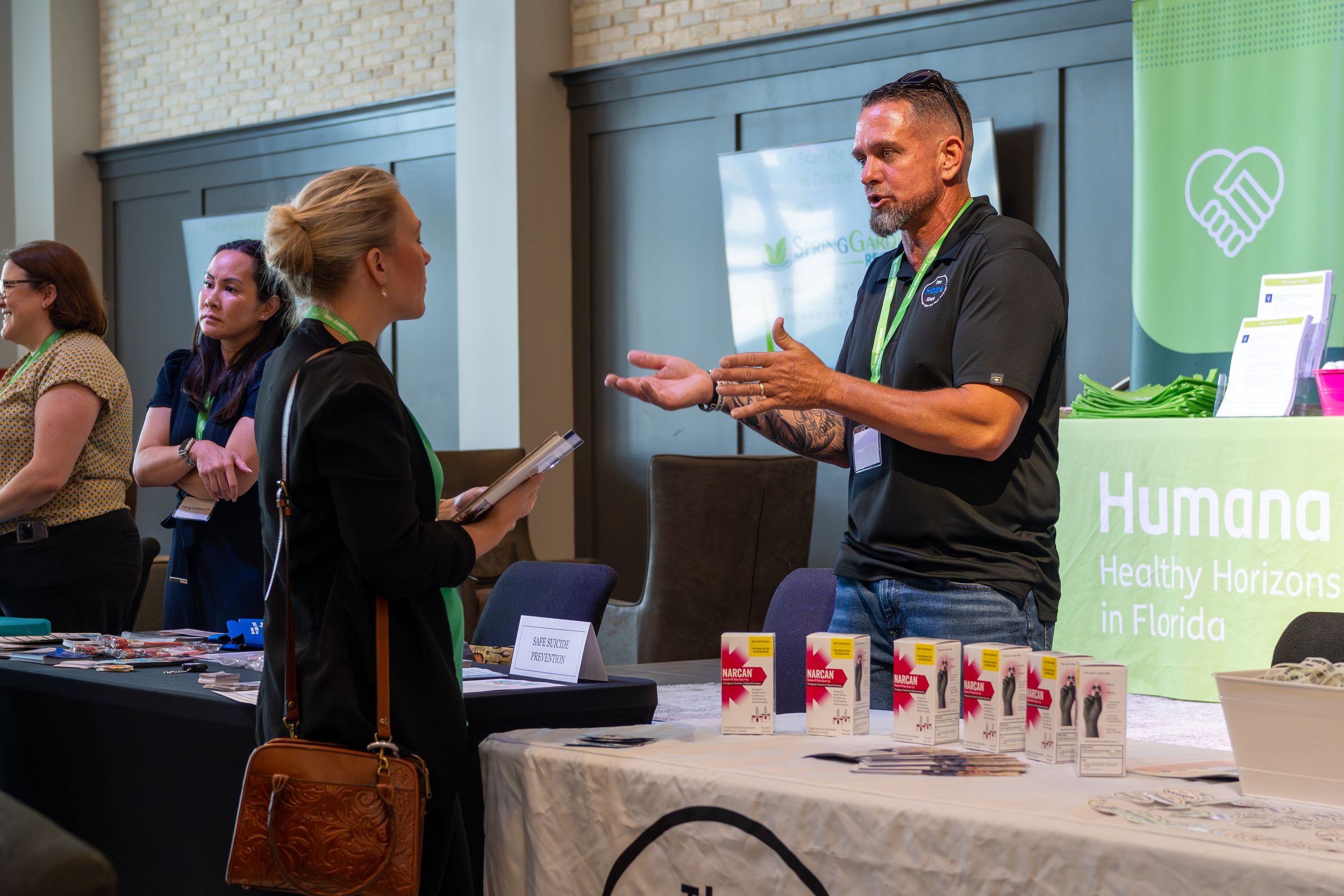 Exhibition hall with vendor tables and banners displaying community organization logos.