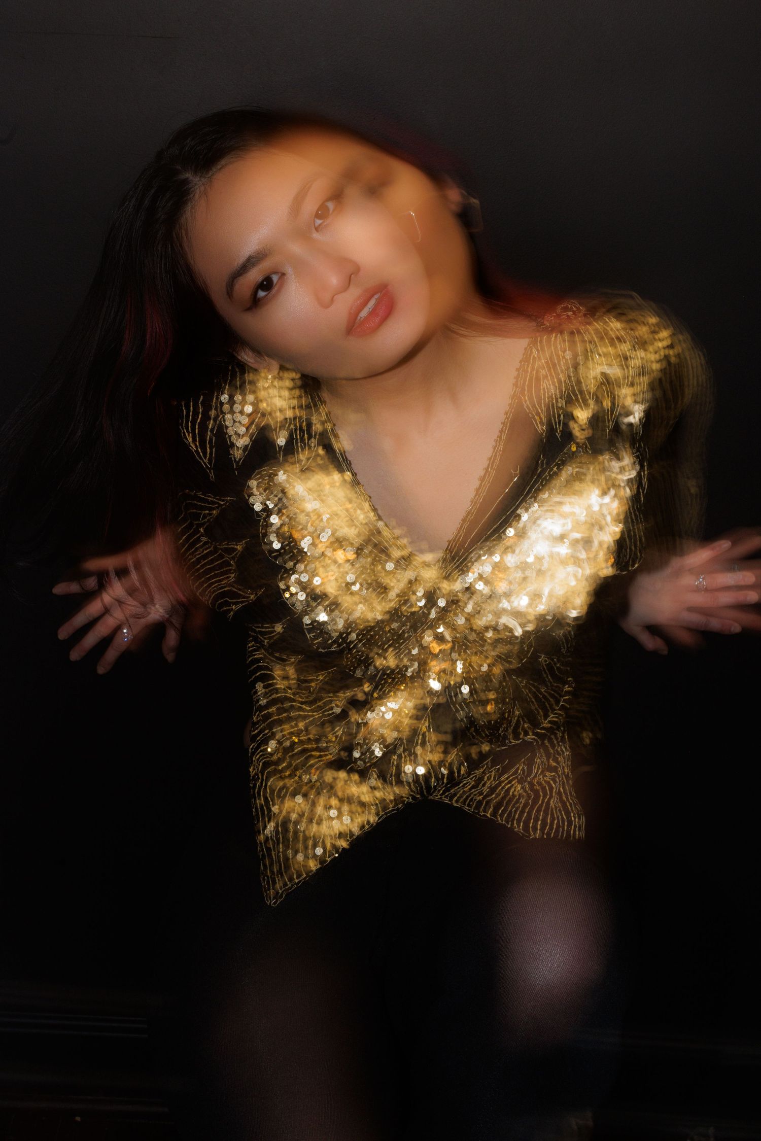 Artistic portrait with a shimmering gold v-neck top in moody lighting.