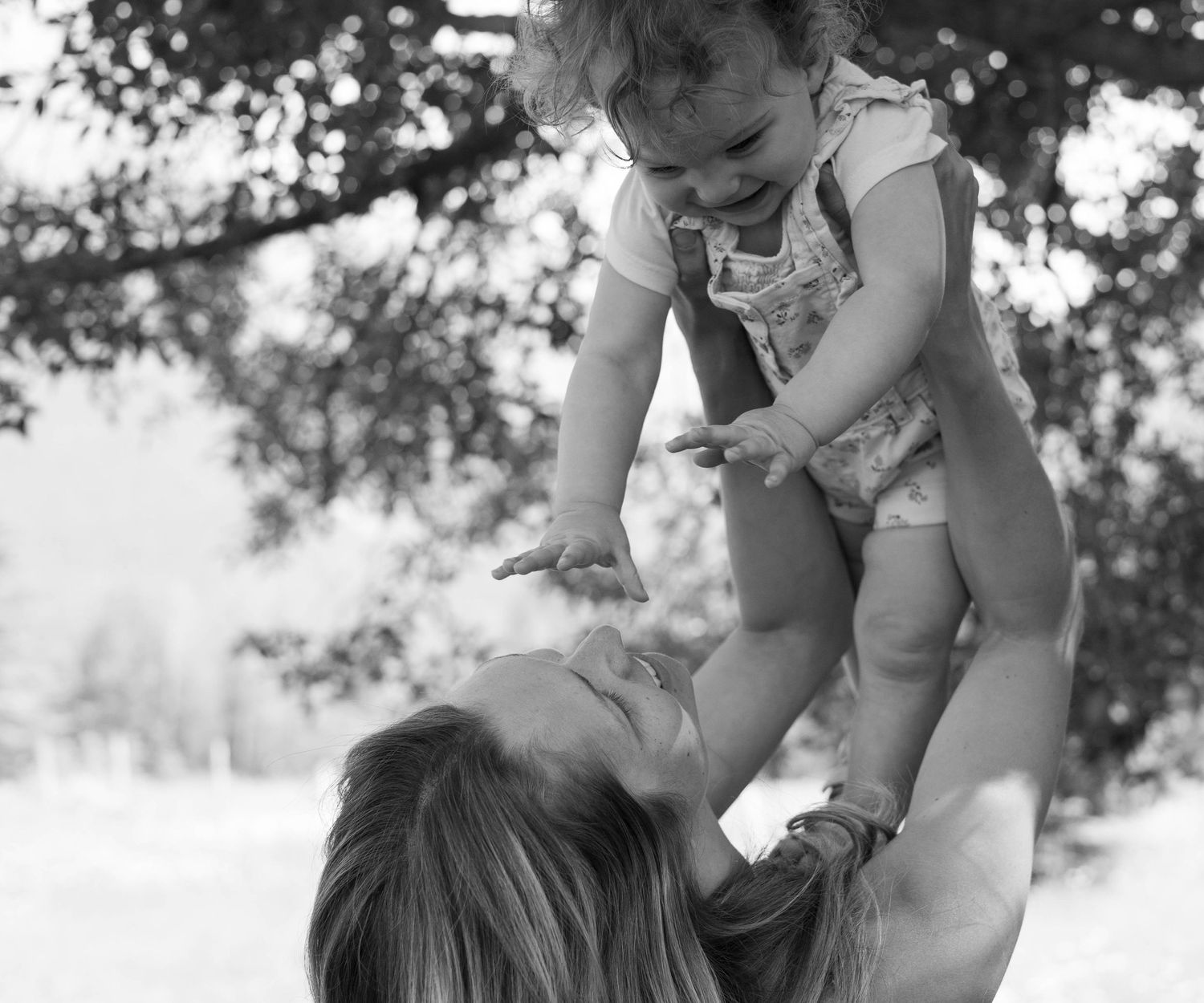 A joyful moment captured in black and white as a baby is lifted high into the air outdoors.