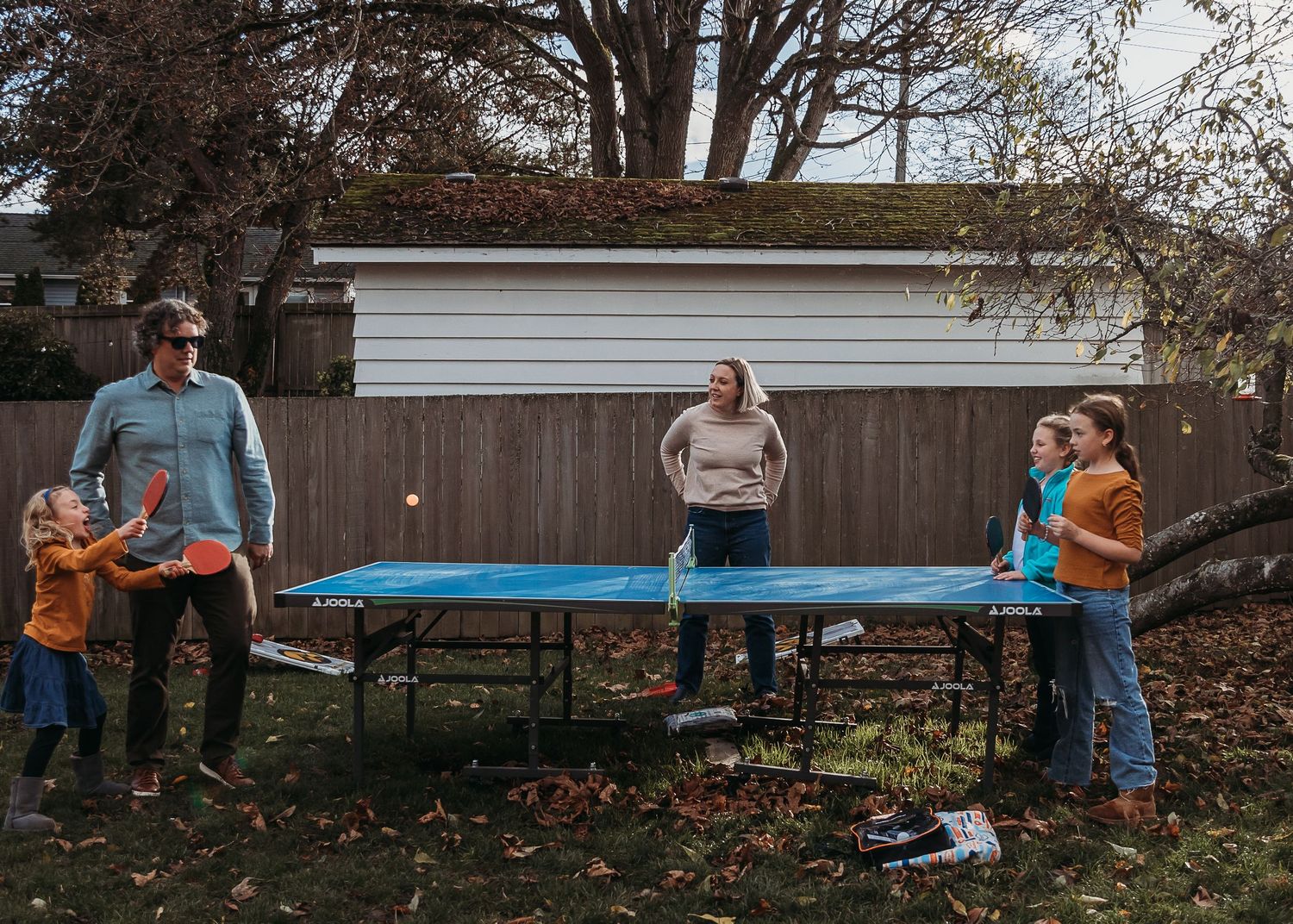 Family playing ping pong together in backyard with trampoline.