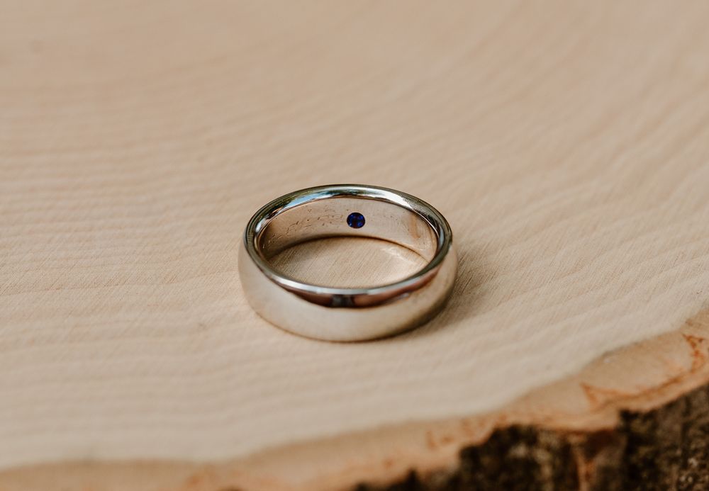 Simple silver wedding band photographed on wooden surface.