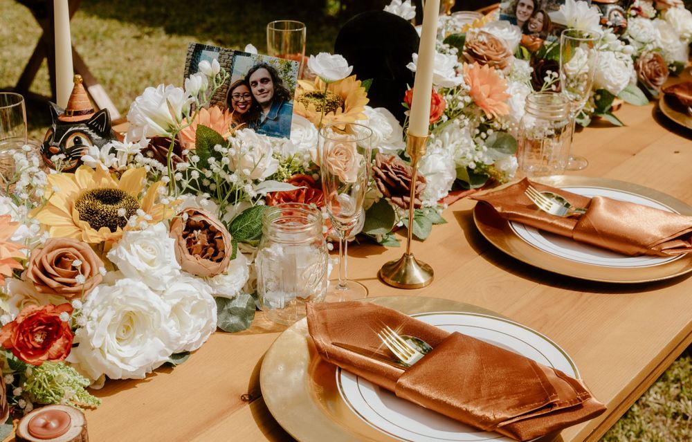 Elegant wedding table setting with peach and white flowers, gold accents, and place settings on a neutral tablecloth.