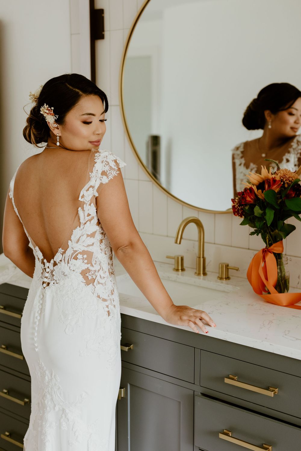 Elegant white lace wedding dress with open back design and floral details in modern bathroom setting.