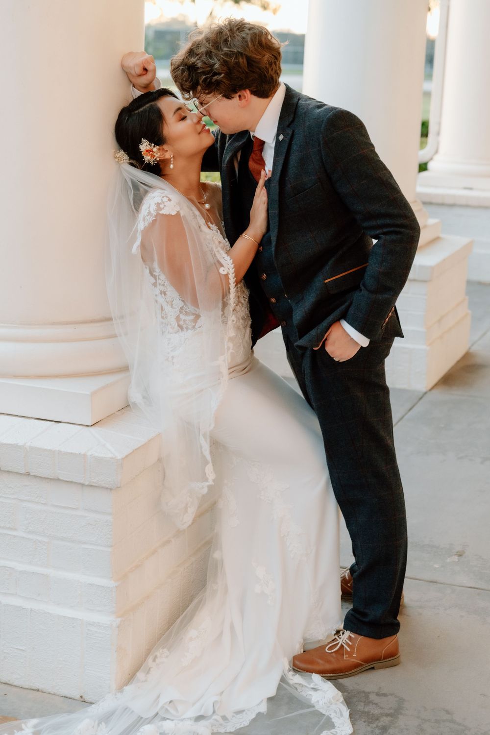 A romantic moment between newlyweds against white pillars on their wedding day.