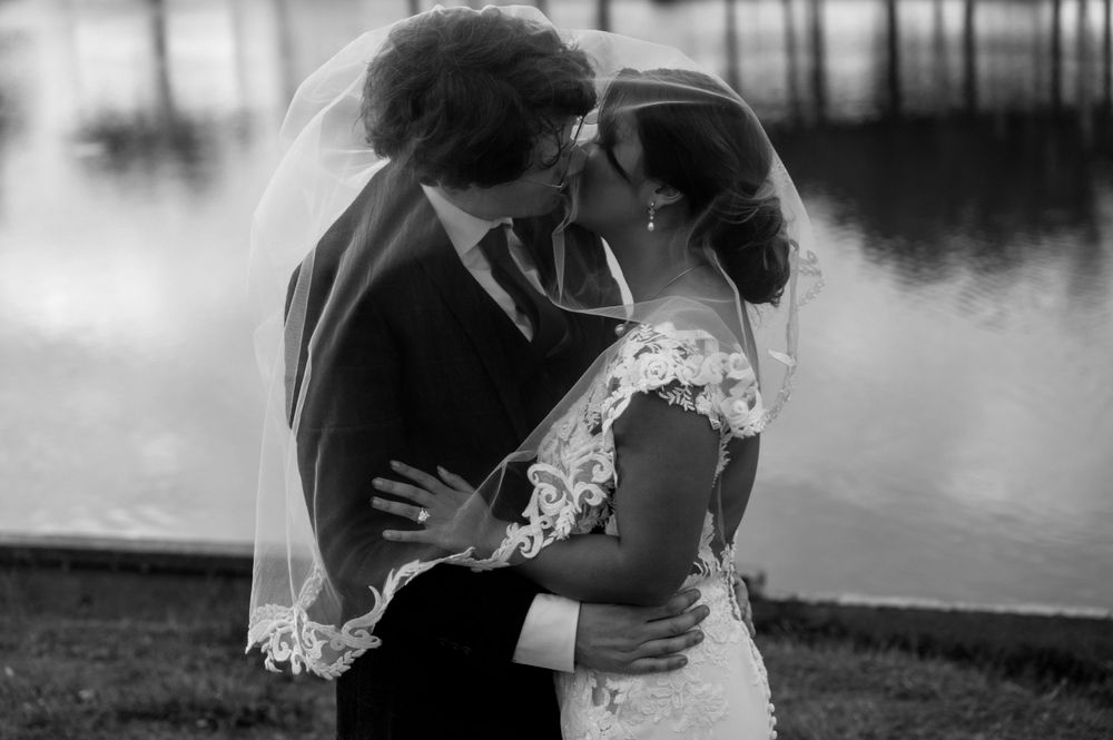 Black and white romantic moment between newlyweds by waterfront at sunset.