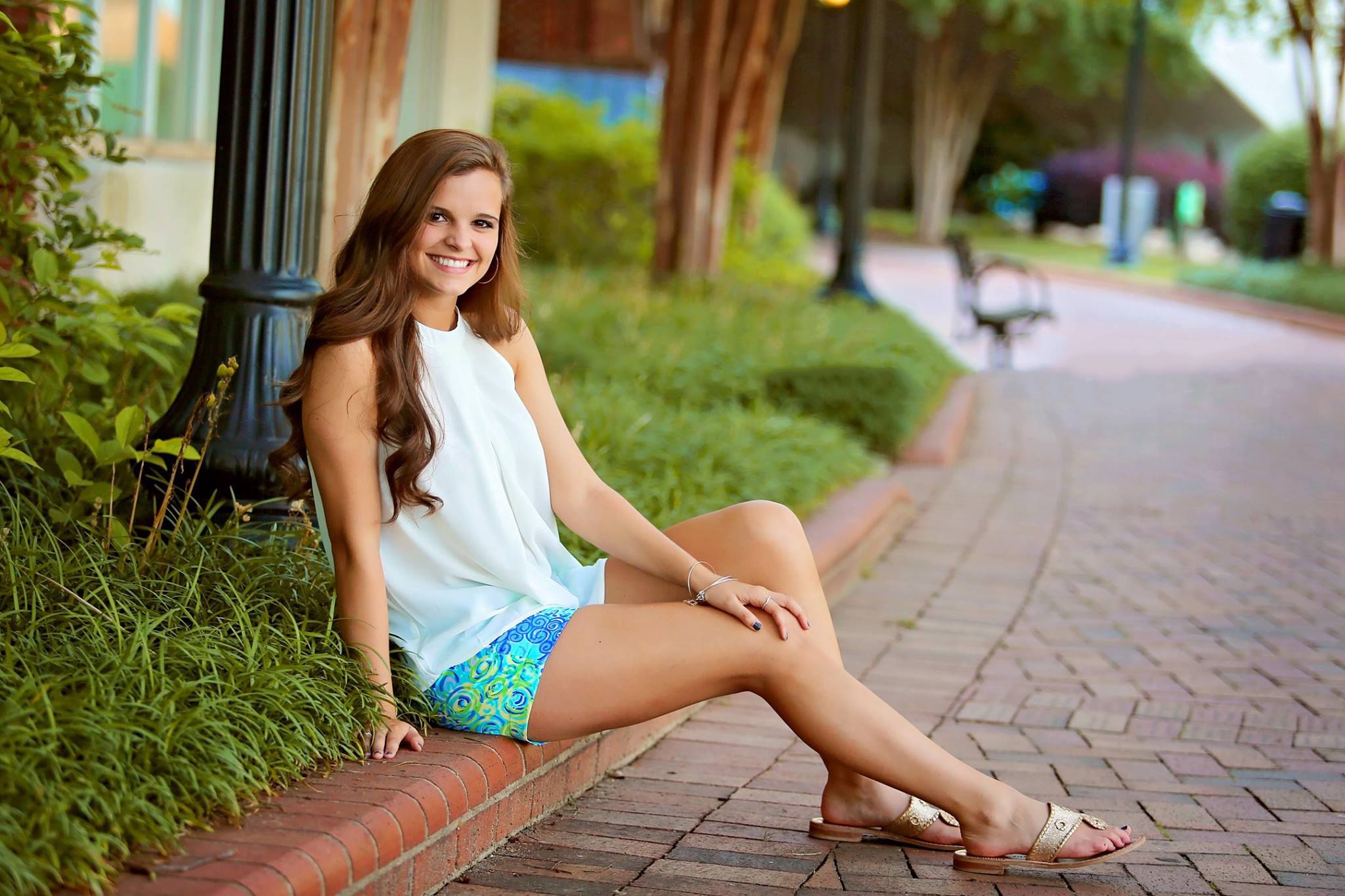 A casual outdoor portrait taken on a brick pathway with lush greenery in the background.