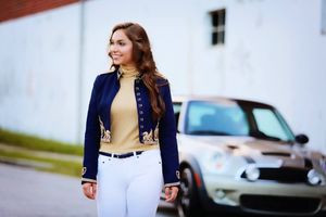 A stylish outfit featuring a navy military jacket with white pants and a beige top near a parked car.