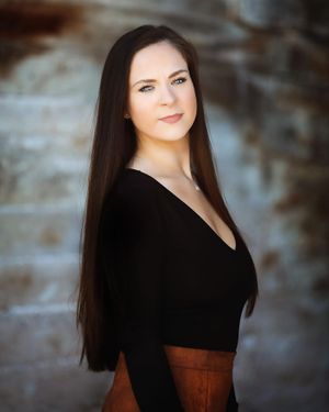 Studio portrait against textured background featuring elegant black top and dramatic lighting.
