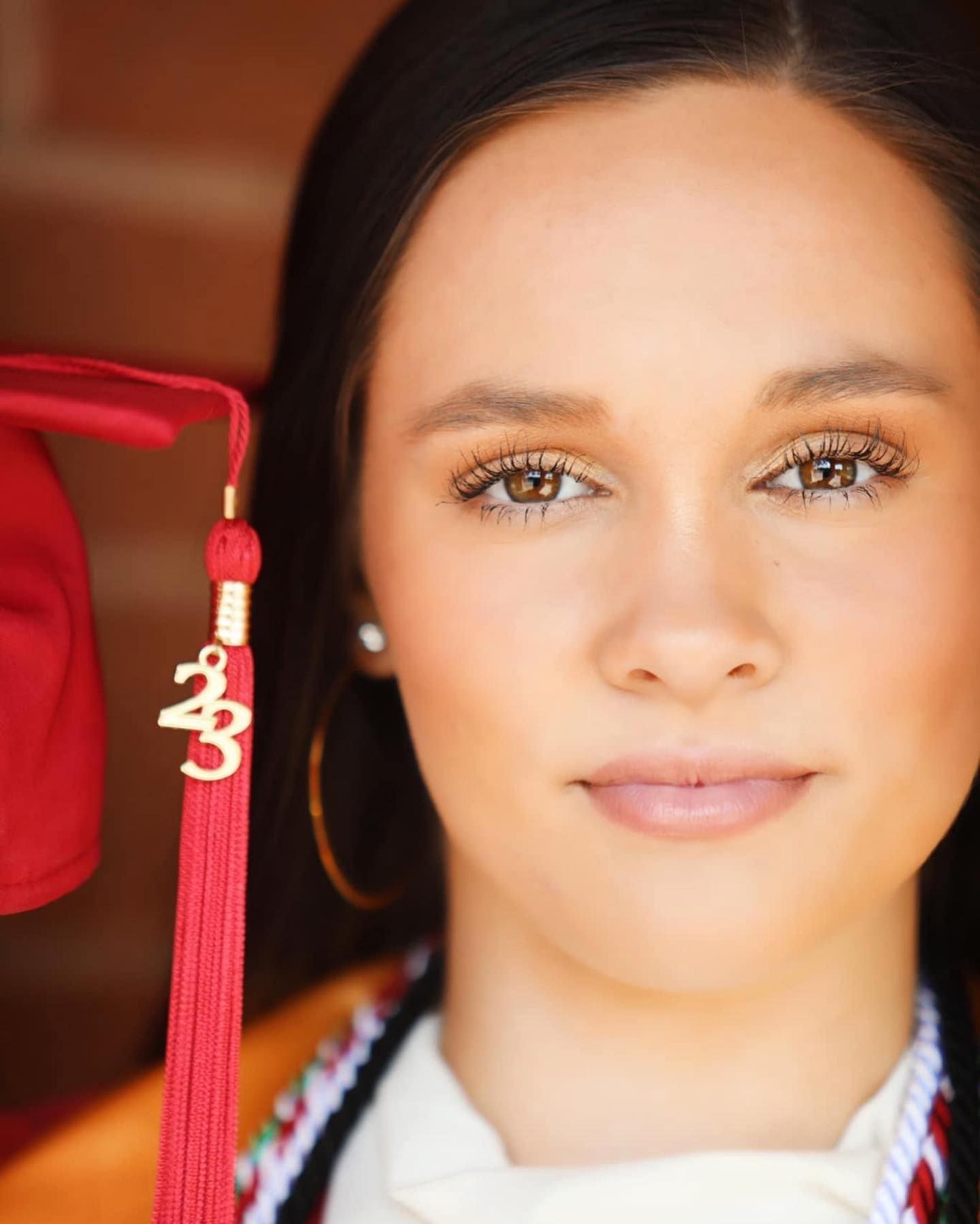 Graduate portrait with red tassel and cap showing natural makeup and pearl earrings.