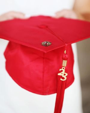 Red graduation cap with tassel and class ring detail on white background.