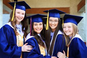 Four graduates in blue caps and gowns pose together smiling in celebration.