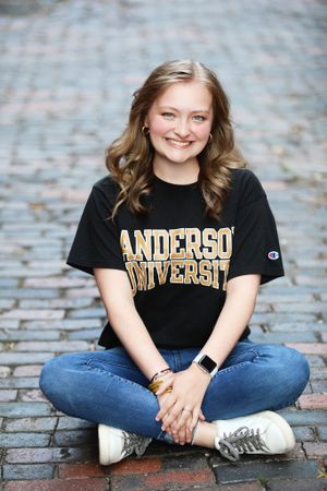 Student in Anderson University t-shirt sits cross-legged on cobblestone path.