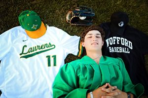 Graduate in baseball attire lies on grass with Wofford baseball gear and jersey.
