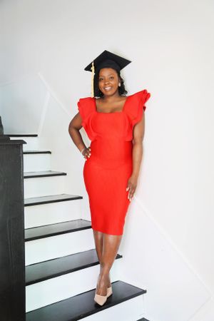 Graduate in bright red dress poses confidently on modern staircase.