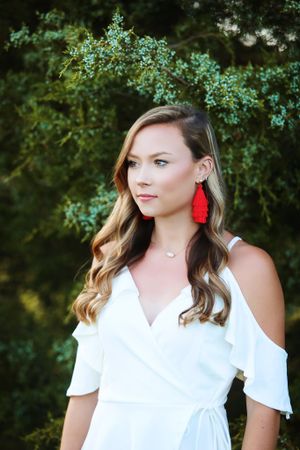 An elegant white dress paired with red statement earrings against a natural green backdrop.